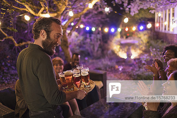 Lächelnder Mann mit einem Tablett voller Biere  der Freunden bei einer Gartenparty serviert