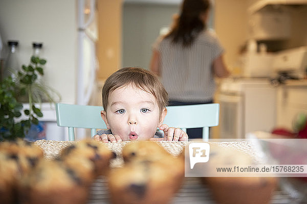 Niedliches  aufgeregtes Mädchen  das sich an frischen  selbstgebackenen Muffins versucht