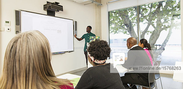 Studenten einer Volkshochschule beobachten den Unterricht ihres Lehrers auf der Projektionsfläche im Klassenzimmer