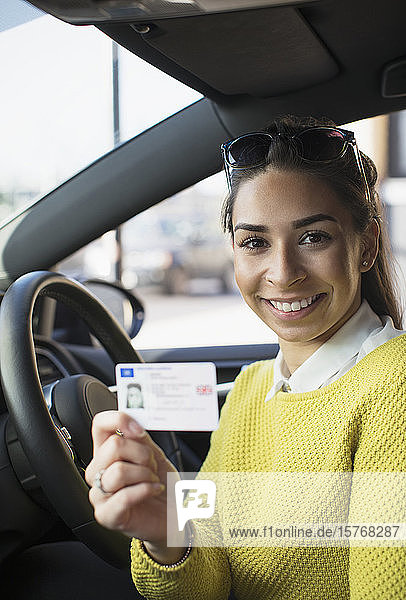Portrait happy young woman holding new drivers license in car