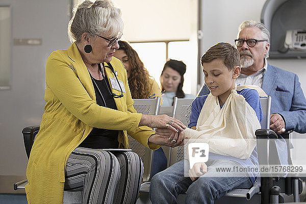 Eine Ärztin untersucht die Hand eines jungen Patienten mit einem Arm in einer Schlinge im Foyer einer Klinik