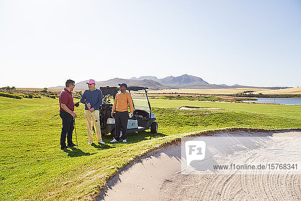 Male golfer friends talking at sand trap on sunny golf course