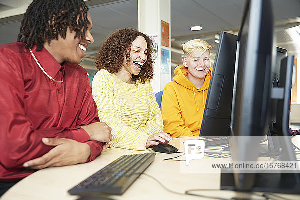 Glückliche Studenten  die gemeinsam am Computer in der Bibliothek lernen