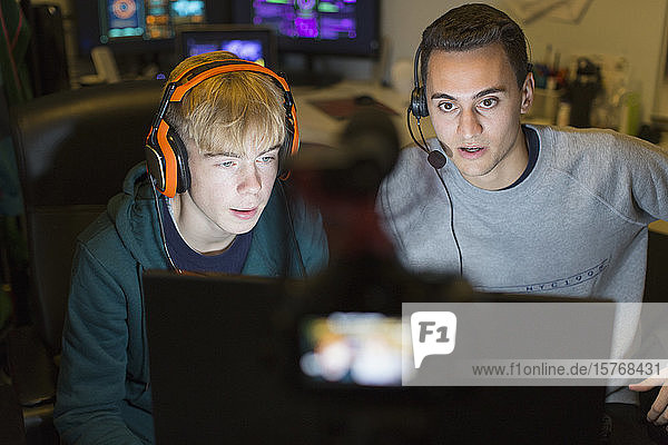 Teenage boys with headphones playing video game at computer in dark room
