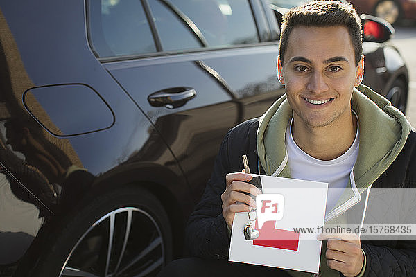 Portrait confident  happy young man holding learners permit by car