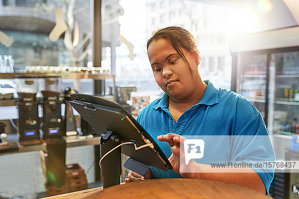Junge Frau mit Down-Syndrom arbeitet an der Kasse eines Cafés
