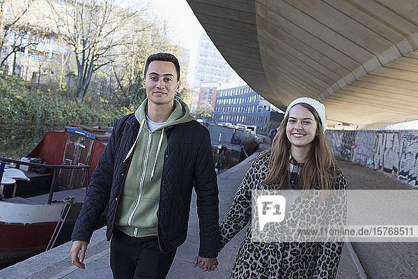 Porträt glückliches junges Paar  das sich an den Händen hält  Spaziergang entlang eines städtischen Kanals