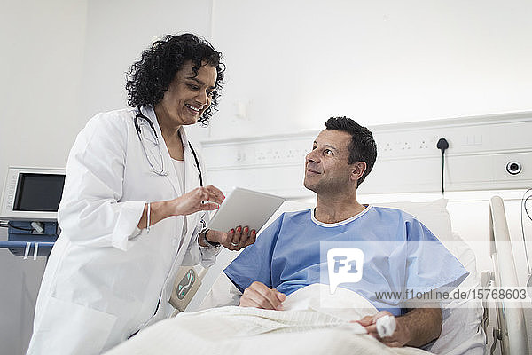 Doctor with digital tablet making rounds  talking with patient in hospital room