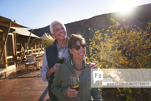 Glückliches älteres Paar trinkt Eistee auf dem sonnigen Balkon einer Safari-Lodge
