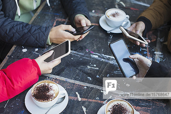 Freunde benutzen Smartphones und trinken Cappuccino am Kaffeetisch
