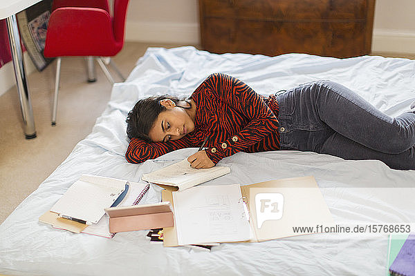 Teenager-Mädchen macht Hausaufgaben auf dem Bett liegend