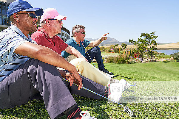 Male golfers resting sitting in grass on sunny golf course