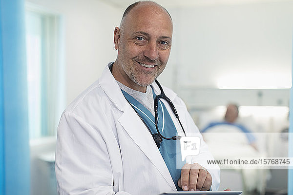 Portrait confident  smiling male doctor using digital tablet in hospital room
