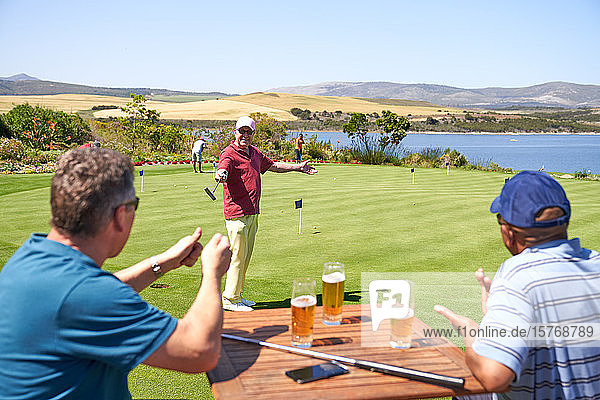 Glückliche männliche Golfer trinken Bier und üben Putten auf dem Golfplatz