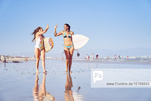 Glückliche junge Surferinnen  die sich am sonnigen Strand die Hände reichen