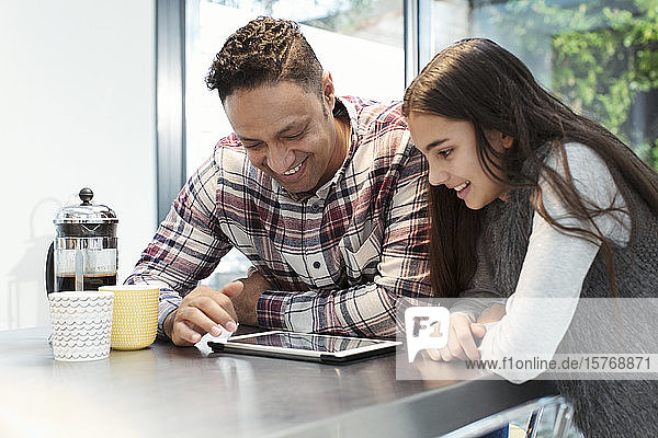 Lächelnder Vater und Tochter benutzen ein digitales Tablet am Küchentisch
