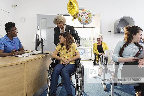 Empfangsdame begrüßt Patientin im Rollstuhl in einer Klinik