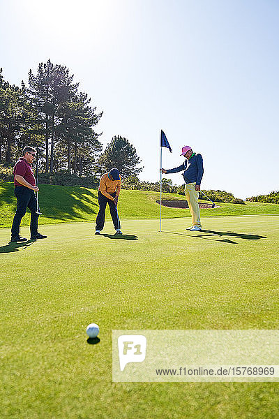Männlicher Golfer beim Einlochen auf dem sonnigen Golfplatz Putting Green