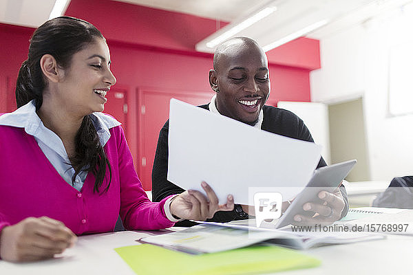 Lächelnde Studenten der Volkshochschule mit Papierkram und digitalem Tablet am Schreibtisch im Klassenzimmer