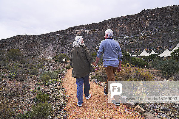 Senior couple holding hands on footpath outside safari lodge cabins
