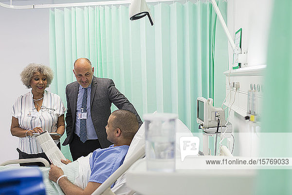 Ärzte bei der Visite  Gespräche mit Patienten  die im Krankenhauszimmer Zeitung lesen