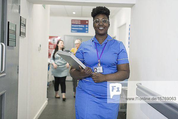 Portrait confident female nurse with medical chart in hospital corridor