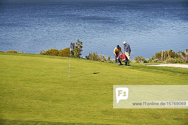 Männliche Golfer planen den Putt auf einem sonnigen Golfplatz am See