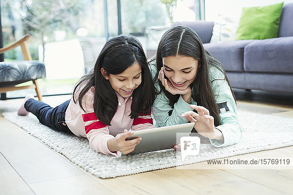 Lächelnde Schwestern mit digitalem Tablet auf dem Wohnzimmerboden