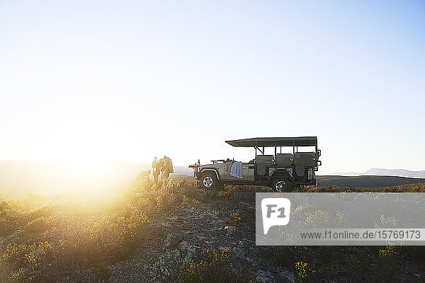 Safari-Gruppe außerhalb des Geländewagens auf einem ruhigen Hügel bei Sonnenaufgang