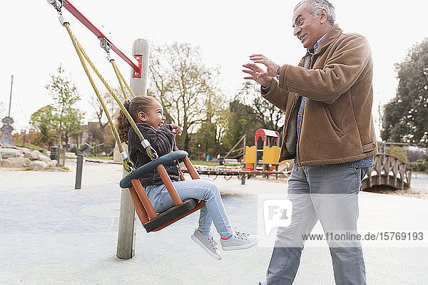 Großvater schiebt Enkelin auf Spielplatzschaukel