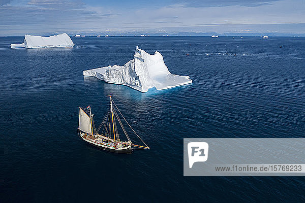 Schiff fährt an majestätischen Eisbergen auf dem sonnigen blauen Atlantik vorbei Grönland