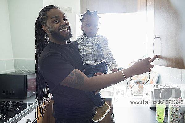 Porträt eines glücklichen Vaters,  der sein Kleinkind in der Küche einer Wohnung hält