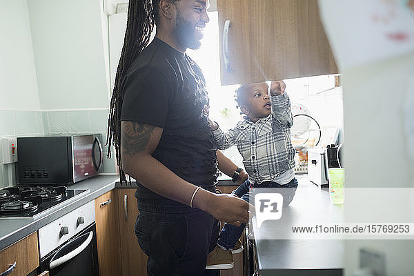 Father and toddler son opening cupboard in apartment kitchen