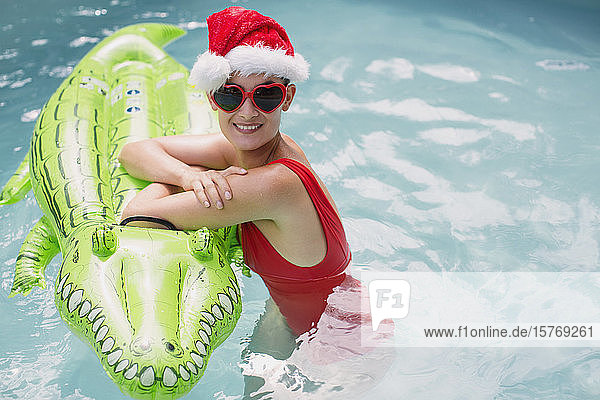Porträt einer selbstbewussten Frau mit Weihnachtsmannmütze und herzförmiger Sonnenbrille  die sich auf ein Floß im Alligator-Pool stützt