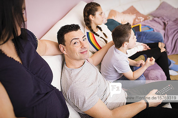 Portrait happy man watching TV on sofa with family
