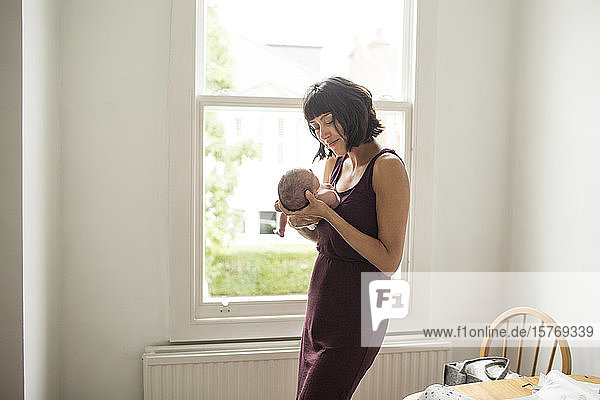 Mother holding newborn baby son at window