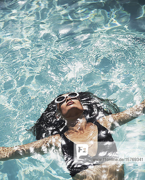 Gelassene  sinnliche Frau mit Sonnenbrille und Bikini schwimmt im sonnigen Schwimmbad