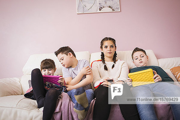 Mädchen und Bruder mit Down-Syndrom benutzen digitales Tablet auf dem Sofa