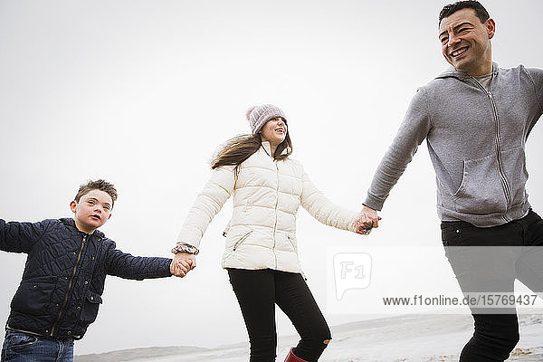 Glücklicher Junge mit Down-Syndrom läuft mit Vater und Schwester am Strand