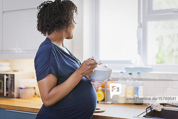 Pregnant woman eating and looking out kitchen window