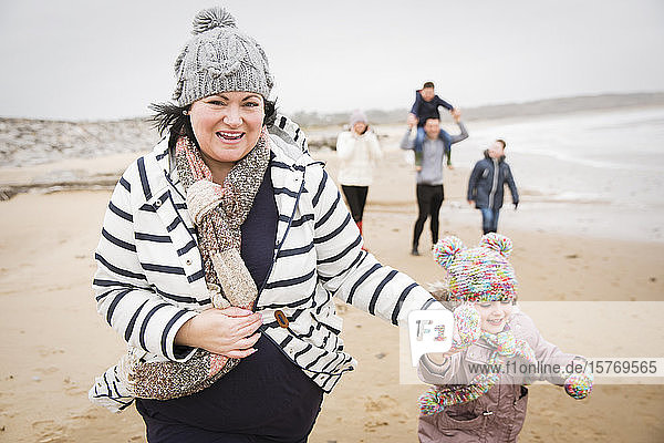 Portrait happy mother and daughter running on winter beach