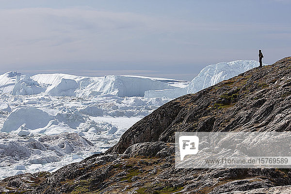 Mann auf Felsen mit Blick auf polare Eisberge Grönland