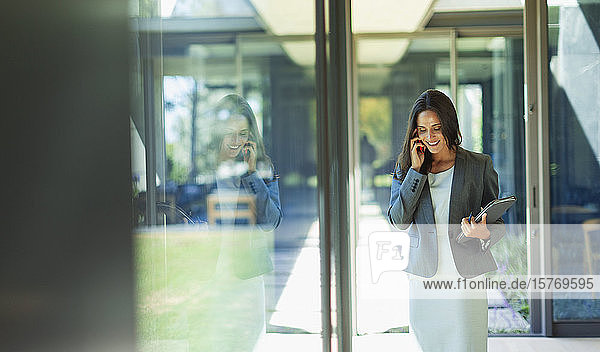 Geschäftsfrau  die in einem sonnigen Korridor mit einem Smartphone telefoniert