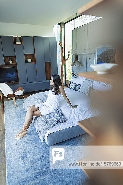 Frau in Handtuch eingewickelt  entspannt auf dem Bett in einem modernen Schlafzimmer