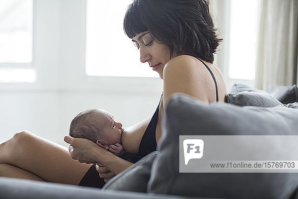 Mother breastfeeding newborn baby on sofa