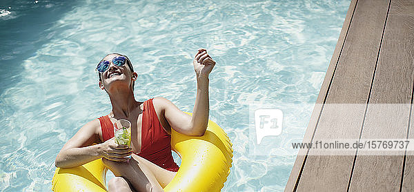 Unbekümmerte Frau mit aufblasbarem Ring trinkt Cocktail im sonnigen Schwimmbad