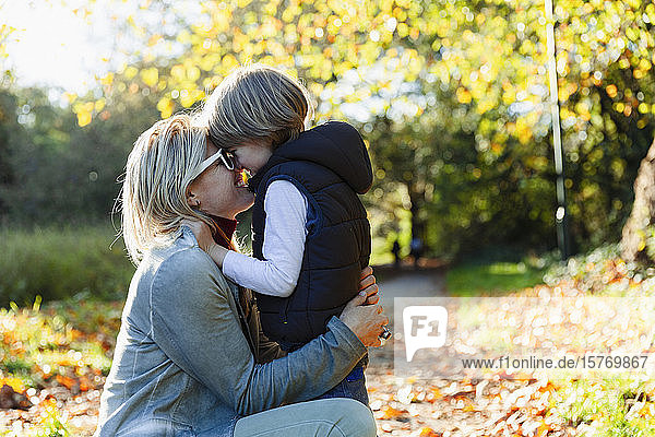 Zärtliche Mutter und Sohn umarmen sich im sonnigen Herbstpark