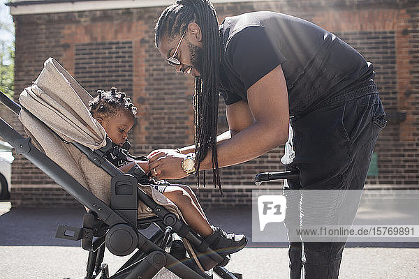 Vater  der sein Kleinkind im Kinderwagen auf dem sonnigen Bürgersteig festhält