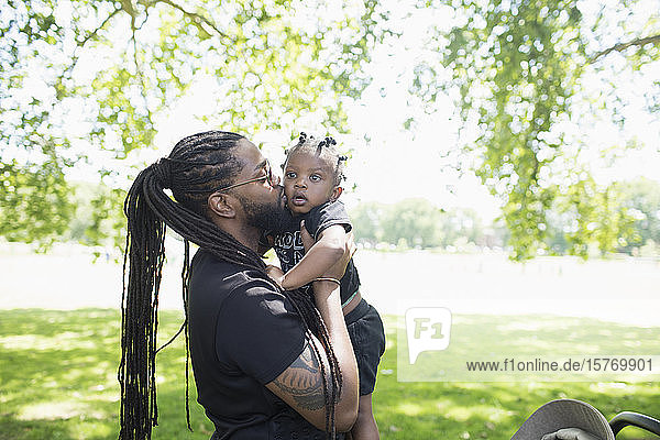 Father with long braids kissing toddler son in park