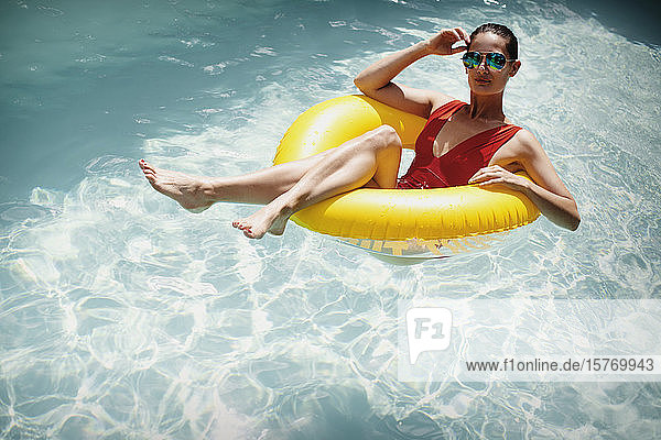 Porträt selbstbewusste Frau entspannt  schwimmt in aufblasbaren Ring in sonnigen Sommer Schwimmbad